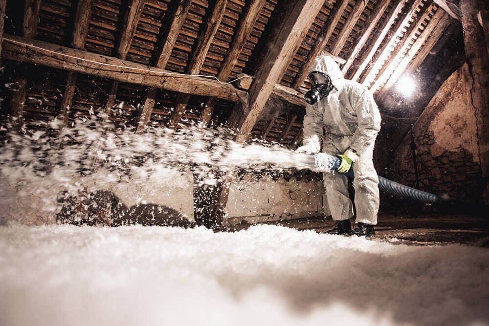 Técnico aplicando lana de vidrio soplada insuflada en buhardilla